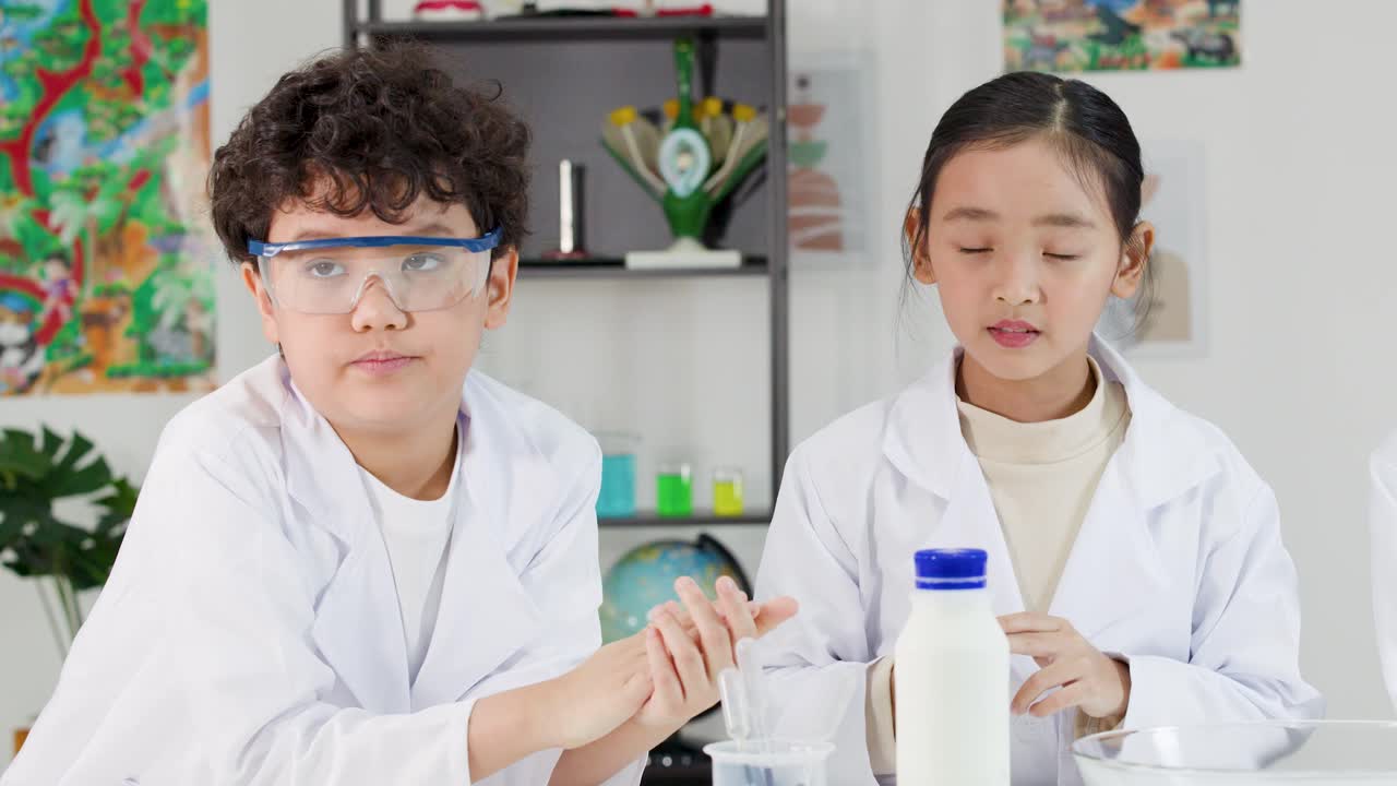 安全ゴーグルと白衣を着た2人のアジア人児童が、学校で化学実験を行っている。