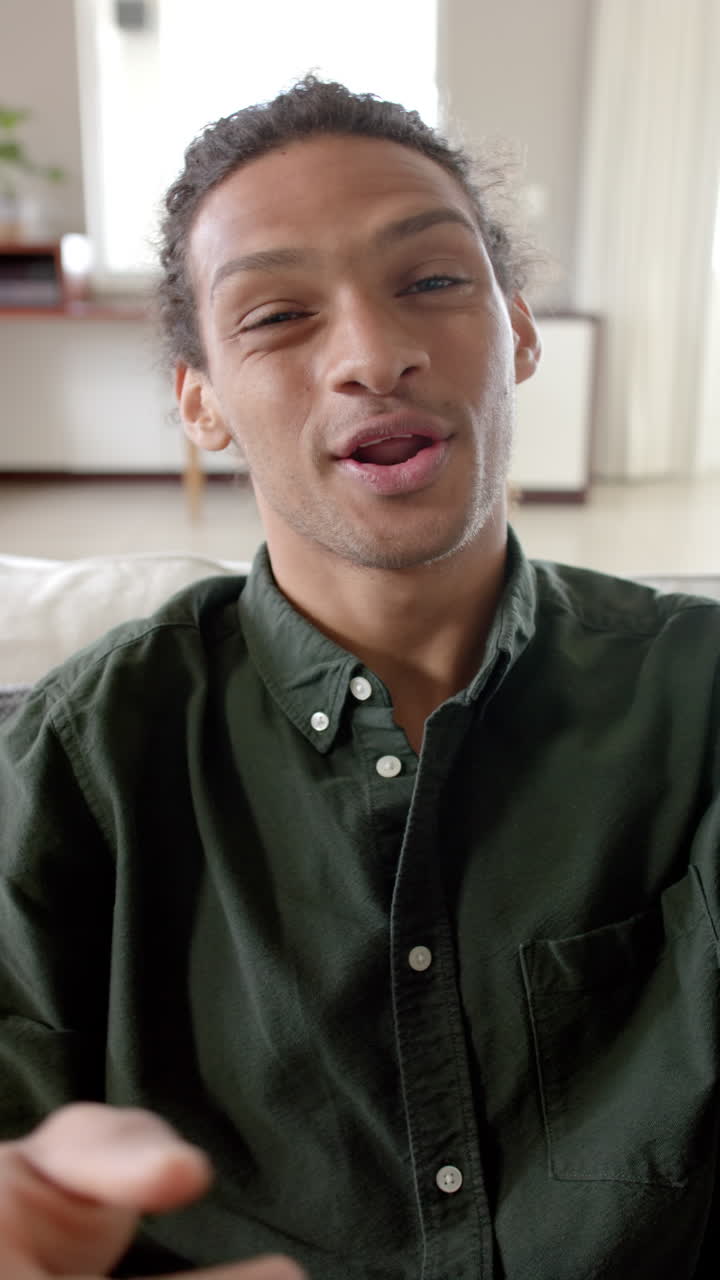 Vertical video of portrait of biracial man talking and having video call at home, slow motion