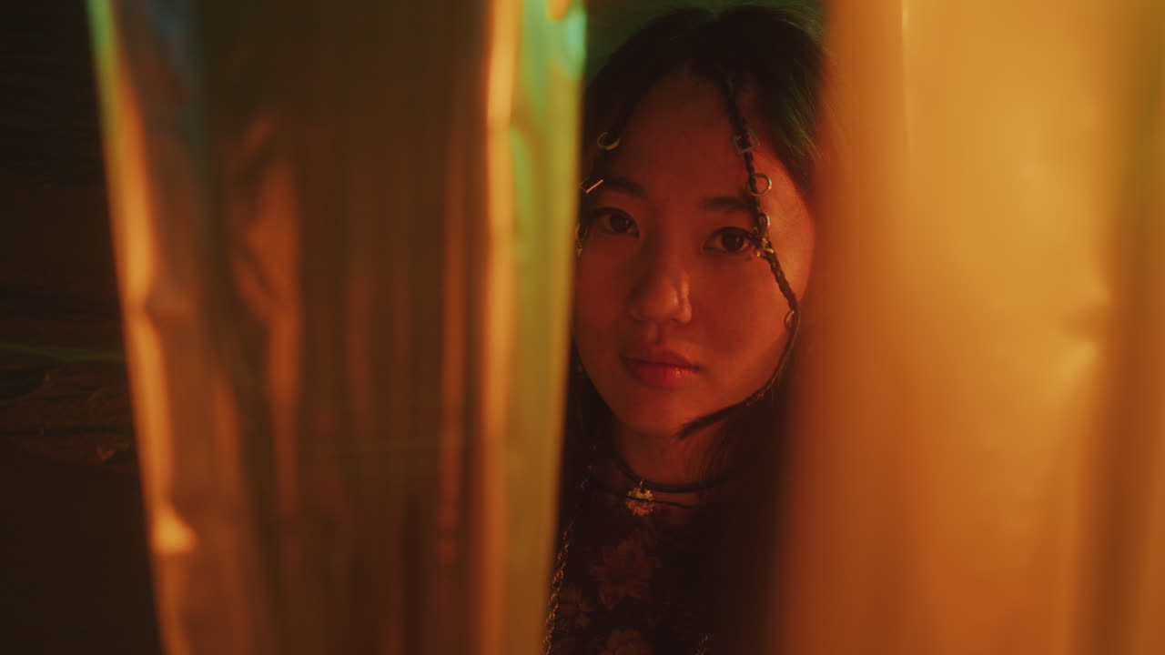 Portrait of Mysterious Asian Beauty among Cellophane Curtains in Neon Light