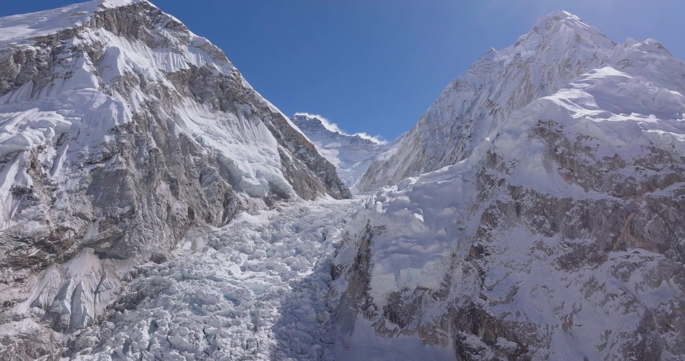 Khumbu Icefall, Everest, Nepal, drone luftoptagelse med langsom svævebevægelse over de brudte isformationer, serac'er og gletsjersprækker i isfaldsdalen, indrammet af stejle bjergskråninger under en klar blå himmel