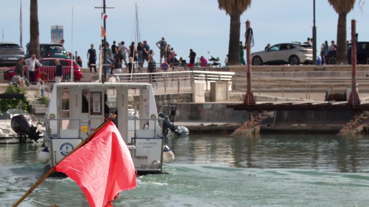 Cassis, Fransa'da kırmızı bayraklarla süslü güneşli bir Akdeniz marinasından ayrılan beyaz bir gezi teknesi.