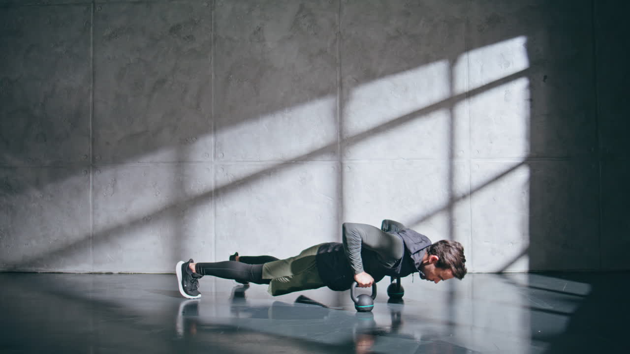 Strong model holding weights equipment standing plank at grey wall background