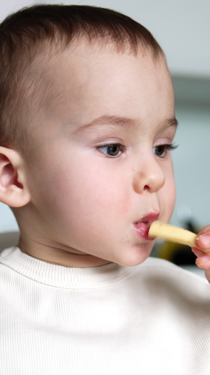 Beautiful child eating porridge from spoon. Cute little boy grabs a piece of cheese and takes a bite. Close up. Vertical video