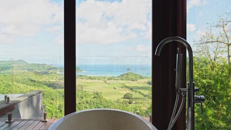 Freestanding-stone-bathtub-with-scenic-views-across-the-mountain-valley-to-Lombok's-southern-Selong-beach