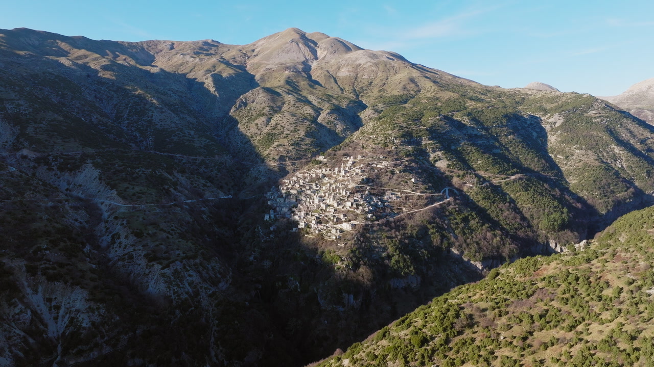 Slow drone reveal shot of Syrrako village in Tzoumerka, Epirus, Greece on a sunny day surrounded by rugged mountains