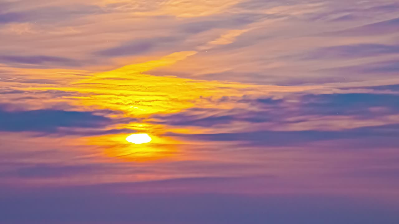 Luftfoto av en levende solnedgang med en glødende oransje og lilla himmel over et tynt skylag. Solen står lavt i horisonten og kaster varme fargetoner over hele bildet.
