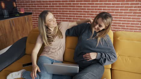 two happy friends with laptop sitting on a couch and hugging