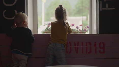 couple of little children looks through window in restaurant