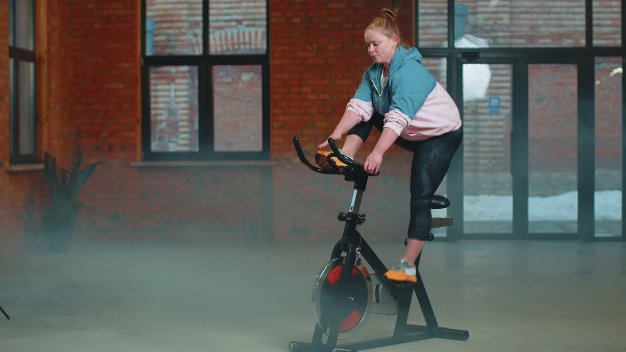 Healthy caucasian woman exercising workout on stationary cycling machine bike in gym slow motion
