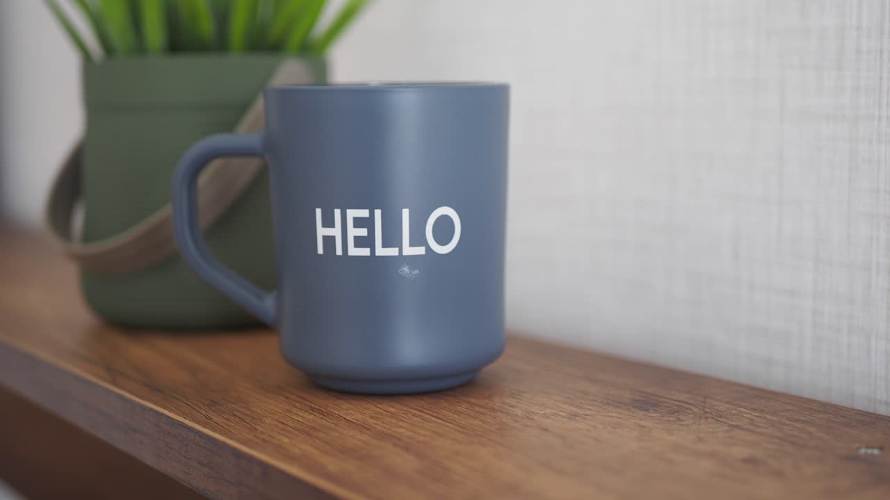 taza gris con la palabra "hola" en un estante de madera