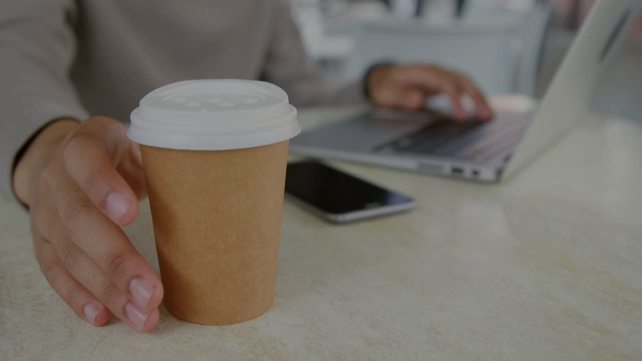 Adult male adjusting cup then typing on laptop, causing blue charts and code overlaying tech desk