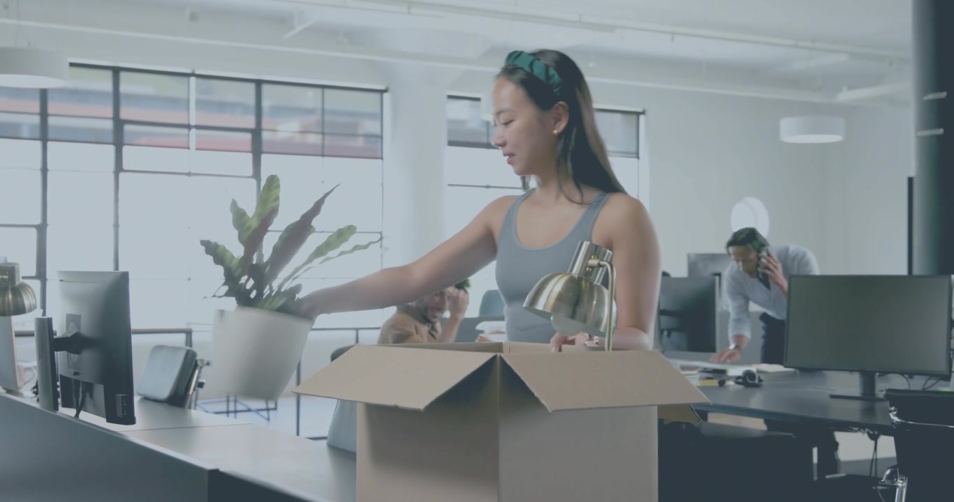 woman carrying box entering office retrieving lamp plant arranging desk while coworker approaching