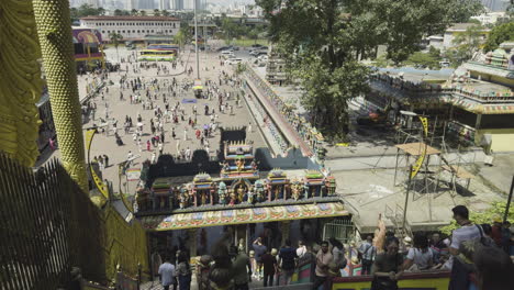 wide overview of crowds visiting batu caves with the giant lord murugan statue and colorful stairs leading up to the temple