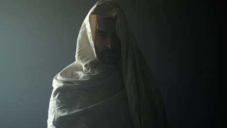 jesus christ resurrected on easter sunday inside empty tomb in bright, shining light and contrasting darkness, wearing white hood and robe. cinematic christian visual.