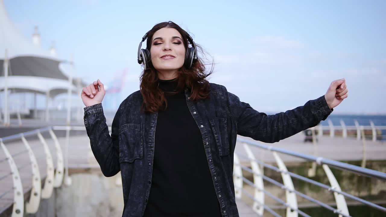 una joven increíblemente atractiva está caminando cerca de la playa con auriculares inalámbricos puestos, bailando y disfrutando de la música. imágenes al aire libre