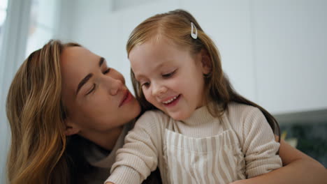 Loving-mother-kissing-child-kitchen-portrait.-Smiling-woman-embracing-daughter