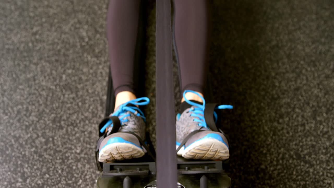 Donna caucasica determinata che si allena con il vogatore in palestra 4k