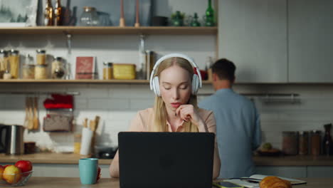 mujer escuchando un curso de entrenamiento sentada en la cocina con auriculares portátiles