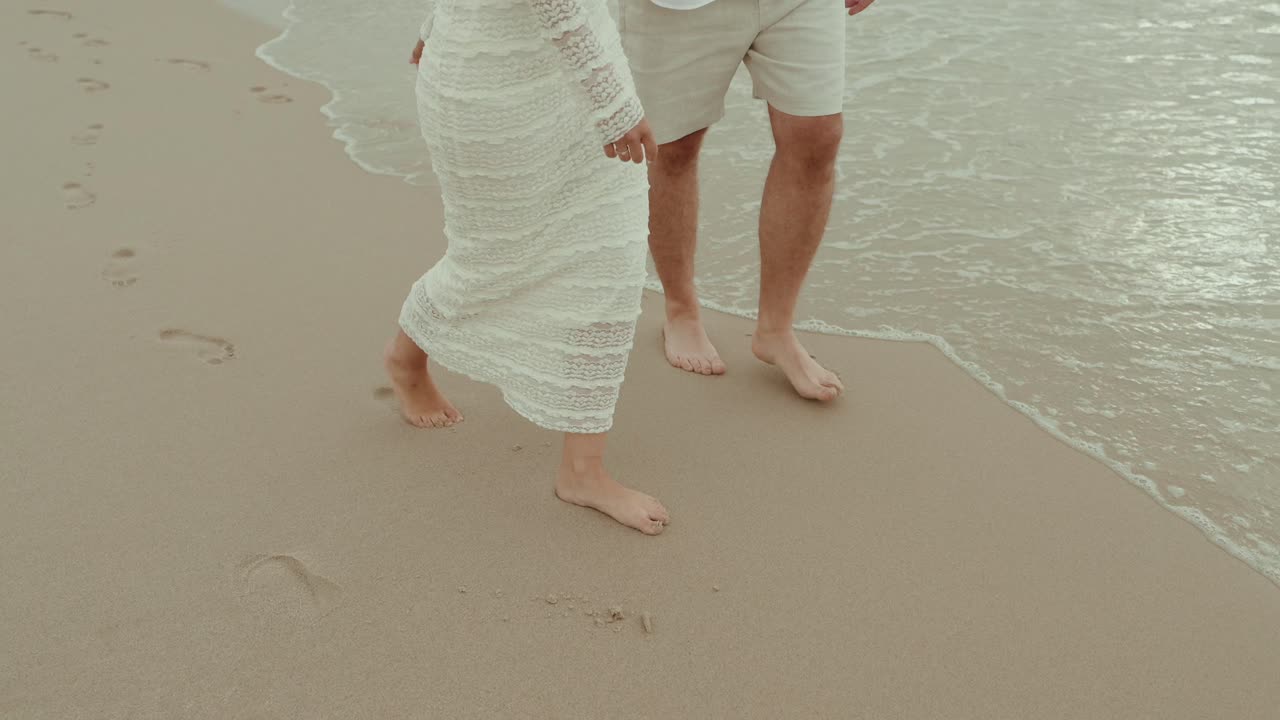 bride and groom walk barefoot along beach leaving footprints in sand