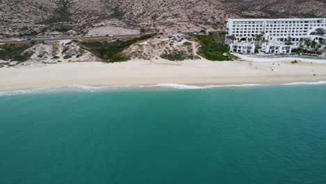 Aerial-View-of-the-beautiful-coastal-shoreline-in-Los-Cabos-with-a-view-of-the-sandy-beach,-a-busy-coastal-road-and-the-turquoise-sea-and-the-renowned-Marquis-hotel-during-a-Mexico-vacation