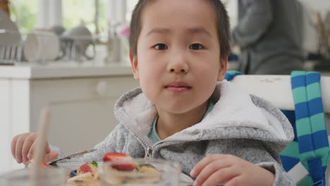 Lindo-Niño-Asiático-Comiendo-Gofres-Frescos-Para-El-Desayuno-Disfrutando-De-Una-Deliciosa-Comida-Casera-Con-La-Familia-En-La-Cocina-De-Casa-4k