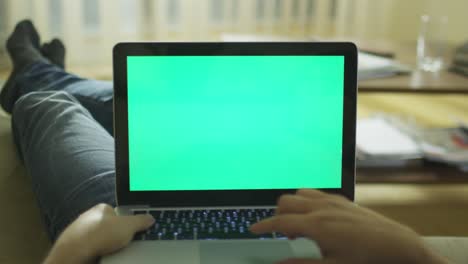 acostado en el sofá en casa usando una computadora portátil con pantalla verde.