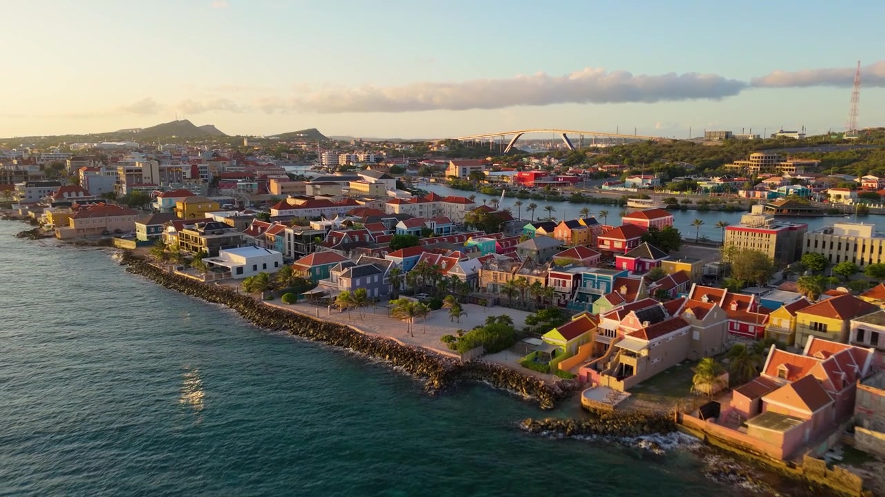 Solnedgang over Pietermaai-distriktet i Willemstad, Curaçao, som fanger kystnært bylandskap og havnefront, tilbaketrekking med bygninger som gløder i gyllent lys