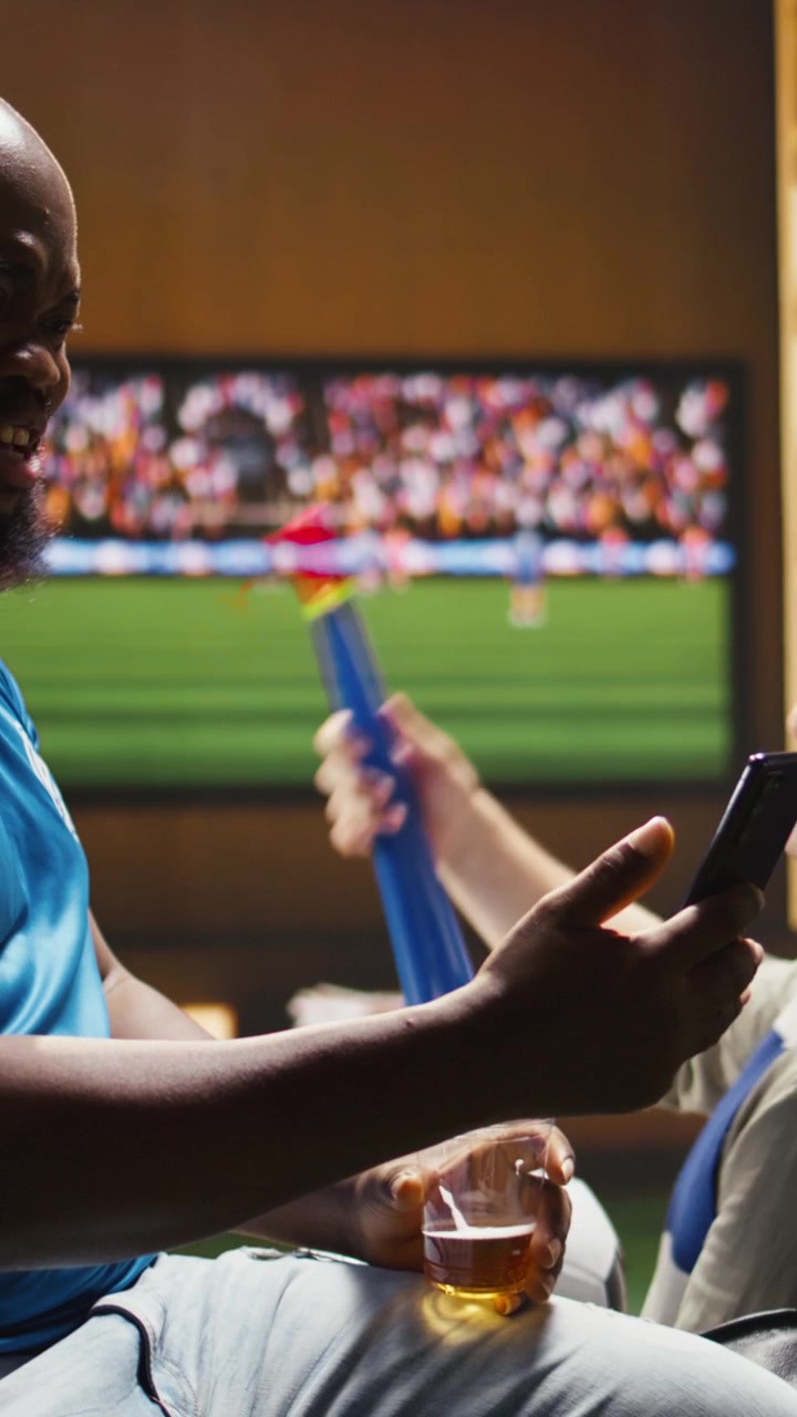 Video verticale. Primo piano di un tifoso di calcio deluso che beve birra e tiene in mano uno smartphone.