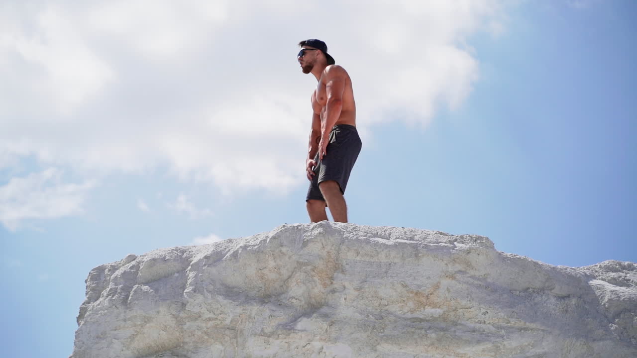 Shirtless athlete with strong body resting after heavy training on the sky background. Muscular man without shirt on white hill outdoors.