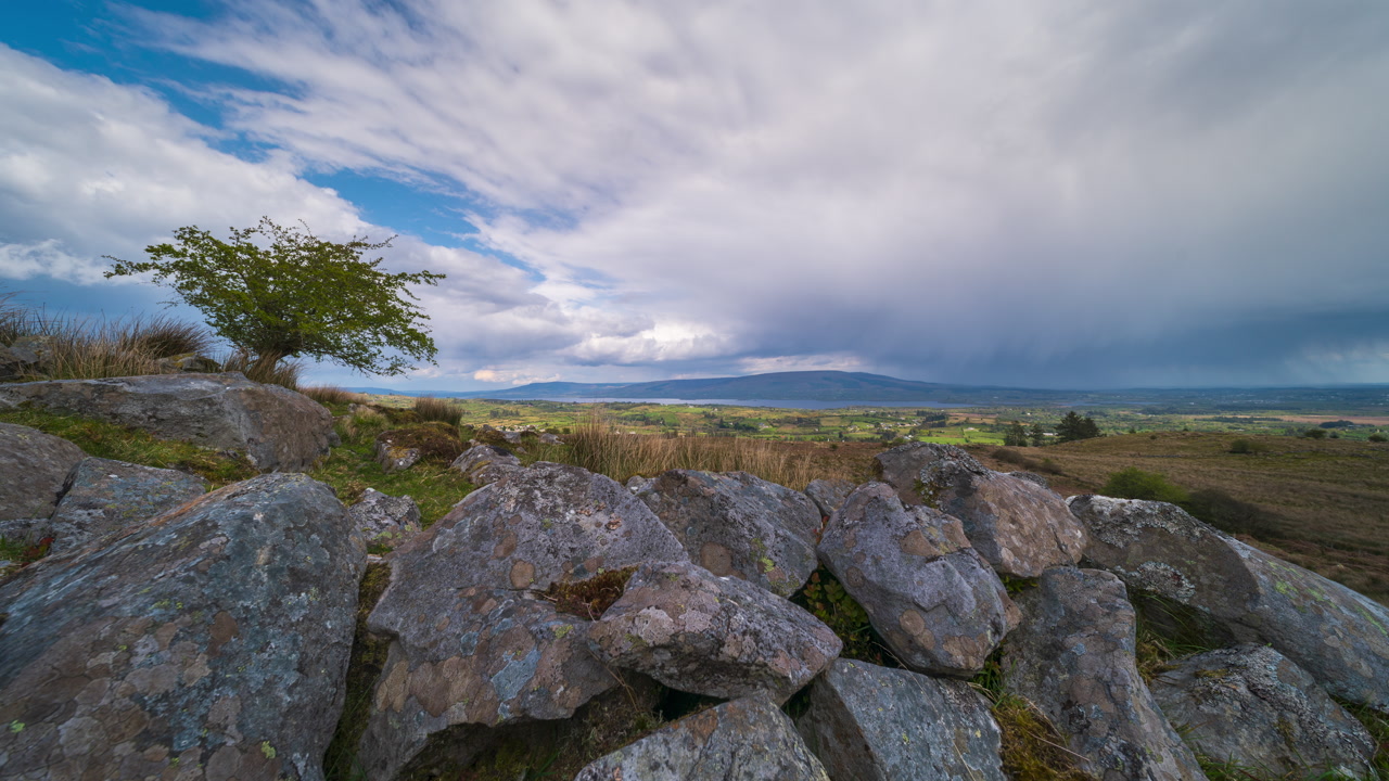 Time lapse of rural landscape with single leafless tree and rocky foreground and hills and lake in the distance on stormy spring day in Arigna mountains in county Leitrim in Ireland.