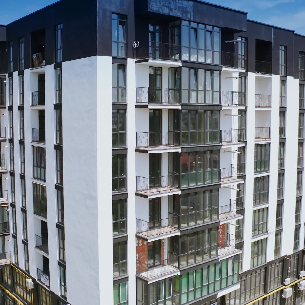 Multi-storey building in white and black colors. Exterior of a tall newly built residential apartment building with many windows and balconies. Camera moving down