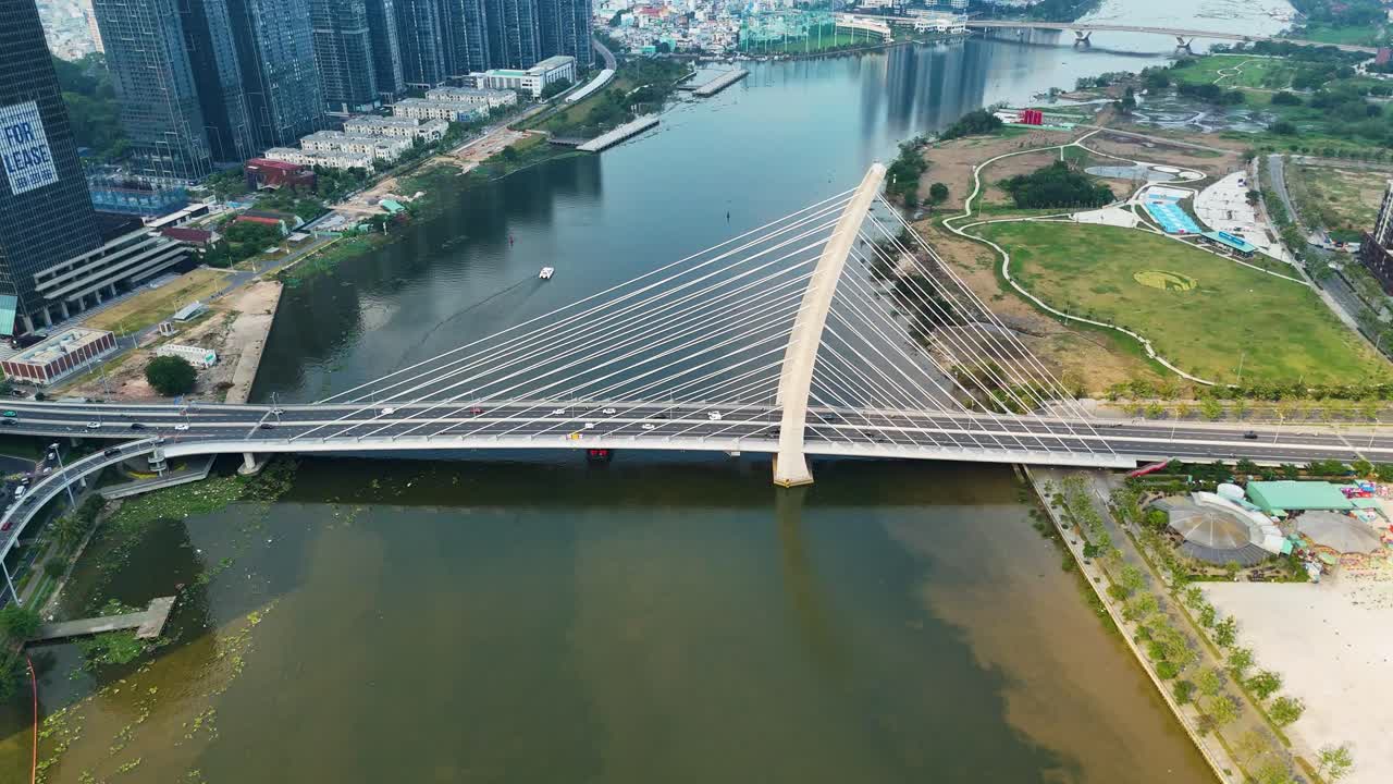 Aerial view of a modern cable-stayed bridge spanning the Saigon River in Ho Chi Minh City, surrounded by high-rise buildings and green urban zones under daylight. Vietnam, UHD.