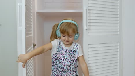 Niña-Pequeña-Con-Auriculares-Escuchando-Música-Y-Bailando-Curiosamente-Cerca-Del-Armario-En-Casa