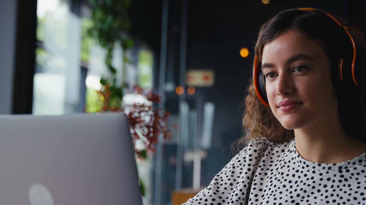 Nærbillede af forretningskvinde med trådløse hovedtelefoner, der arbejder på sin bærbare computer på en café
