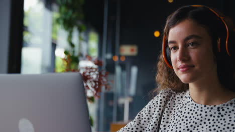 Close-Up-Of-Businesswoman-Wearing-Wireless-Headphones-Working-On-Laptop-In-Coffee-Shop