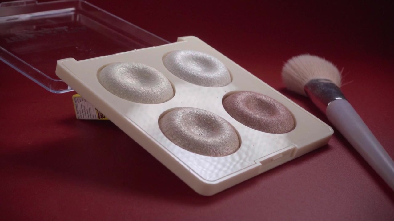 Close-up of makeup brush and neutral eyeshadow palette placed on red background, highlighting soft powder textures and muted shades used for everyday makeup application