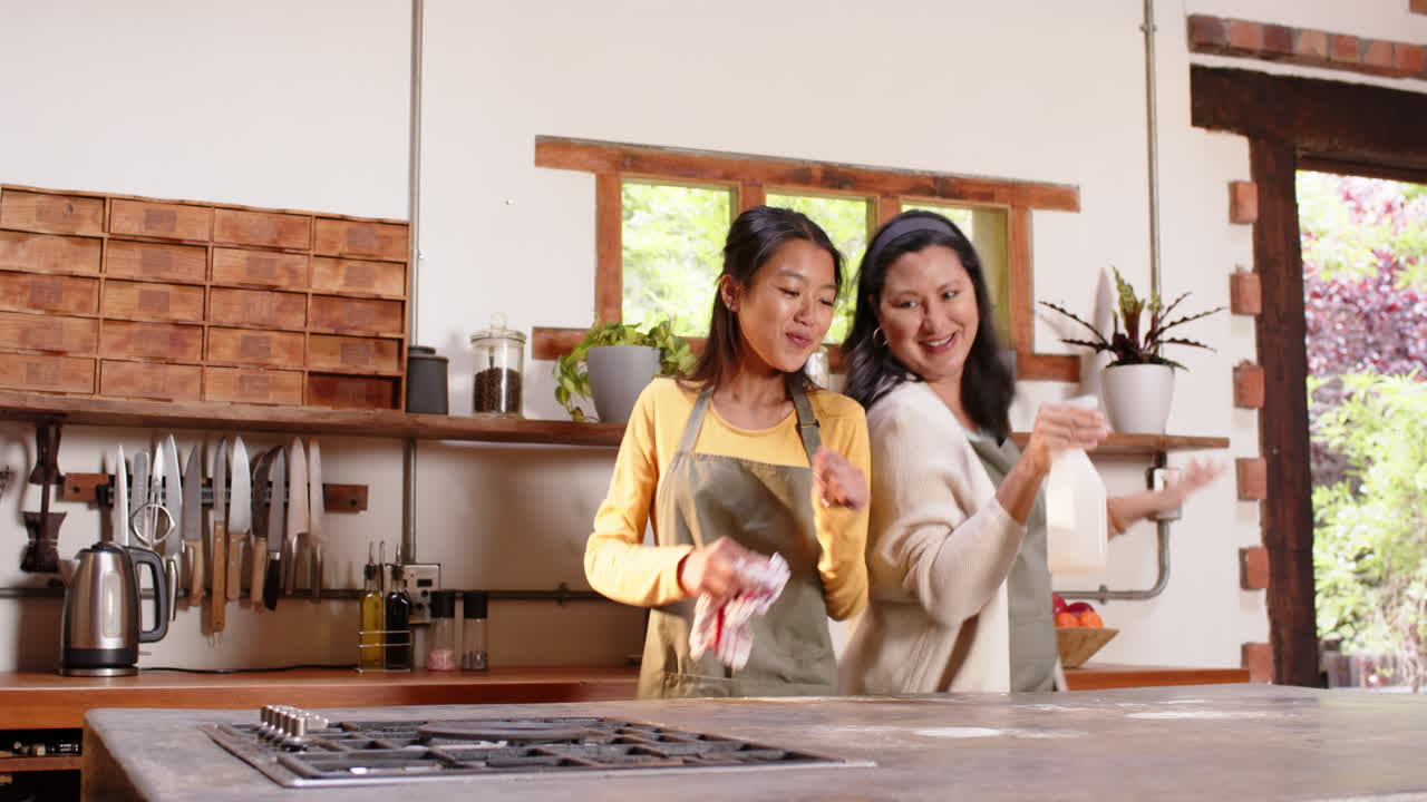 Multiracial grandmother and young woman dancing joyfully in kitchen, at home