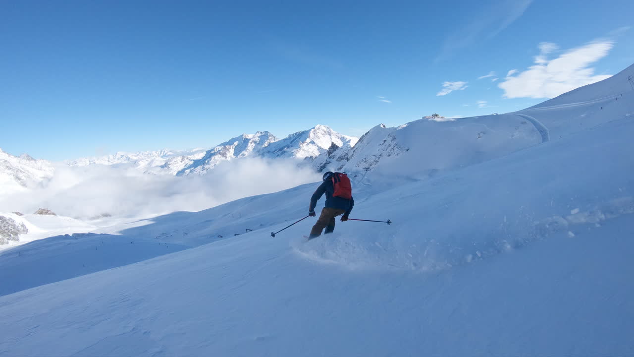 Riprese cinematografiche con telecamera a seguire di sci fuori pista sul ghiacciaio Allalin a Saas-Fee. Curve veloci, crepacci e vasto terreno glaciale in un ambiente alpino svizzero ad alta quota.