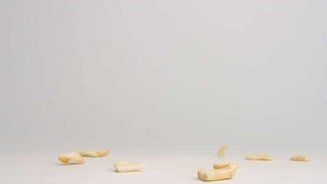 dehydrated dried apple pieces falling onto white table top and bouncing and landing in a pile in slow motion