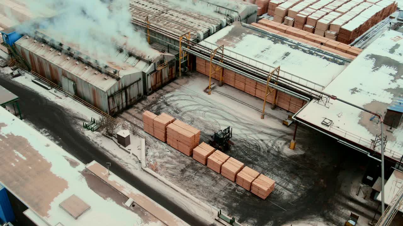 Aerial shot of forklift stacking plywood in front of industrial dry kilns for moisture removal process