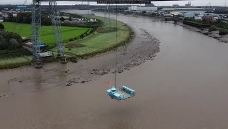 Historic-industrial-Newport-transporter-bridge-platform-moving-across-river-Usk-aerial-birdseye-push-in