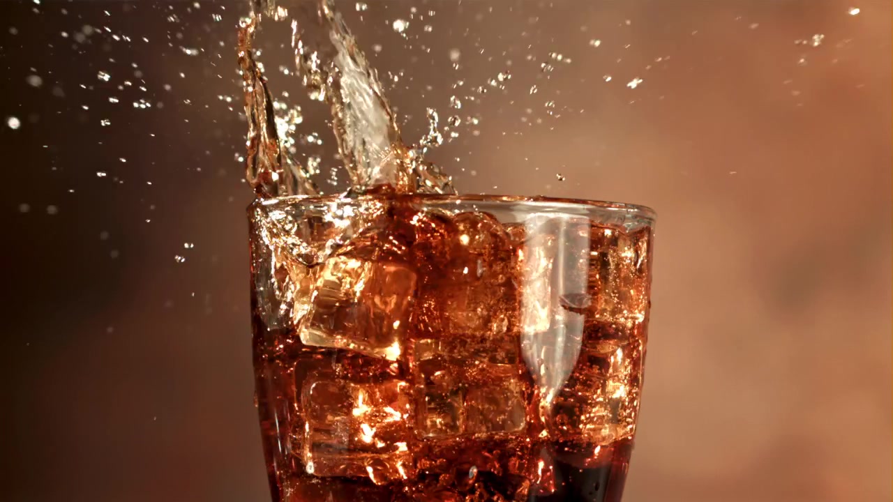 Cubetti di ghiaccio che schizzano in un bicchiere di cola al rallentatore