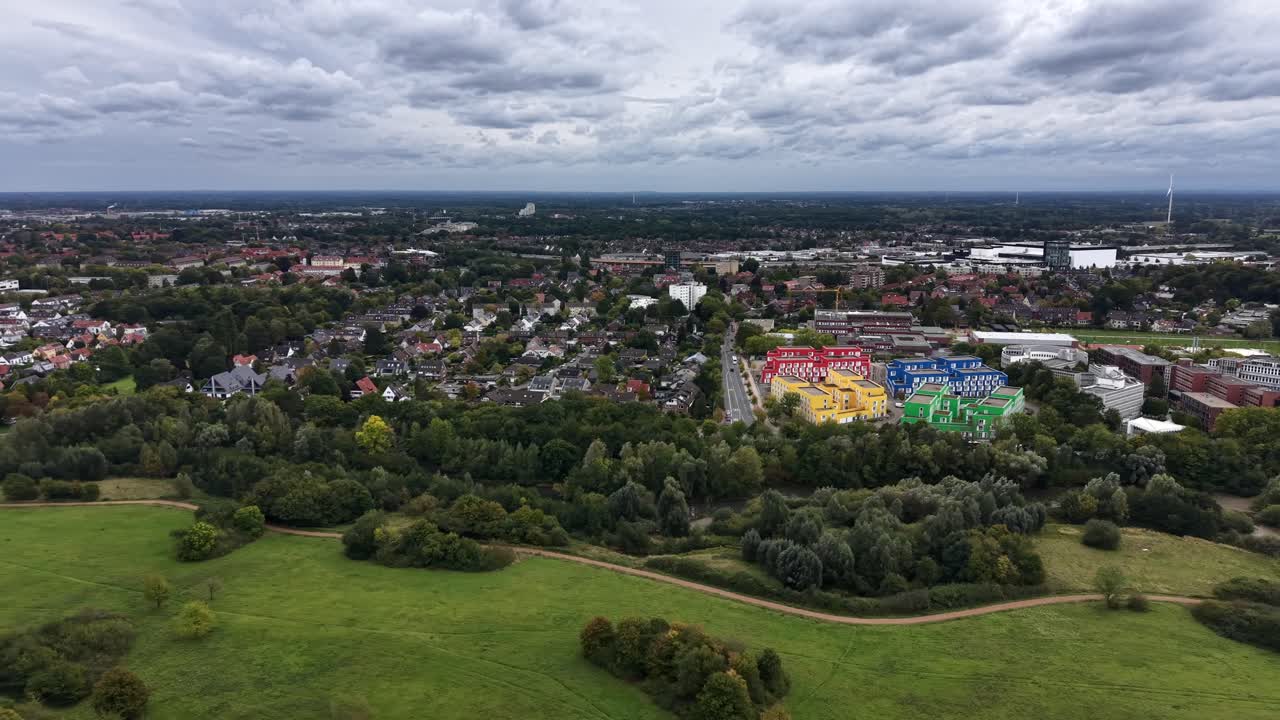 Aerial lateral wide shot of american city with houses and colored apartment complex. Cloudy fall season with colored trees in park with path. Cloudscape at sky