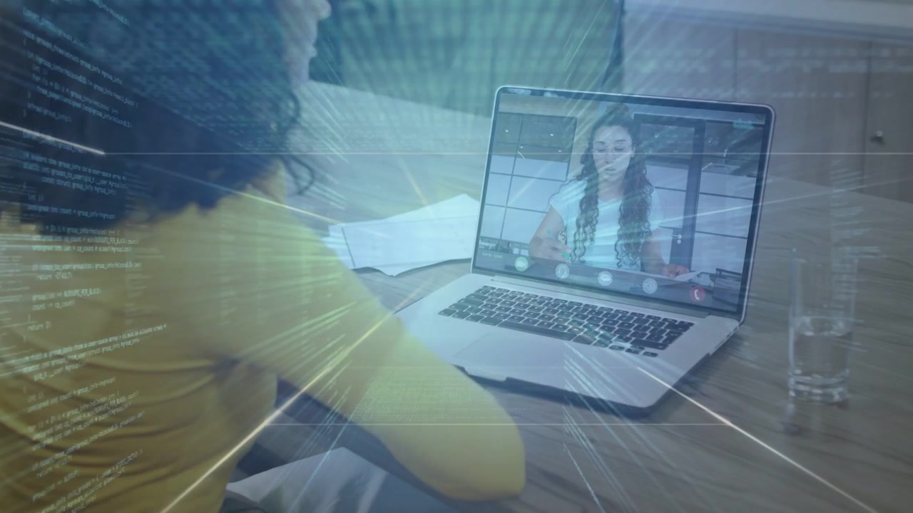 Donna seduta che sposta documenti vicino al laptop mentre un collega sullo schermo parla con un'interfaccia sovrapposta che appare, per una chiamata di lavoro.