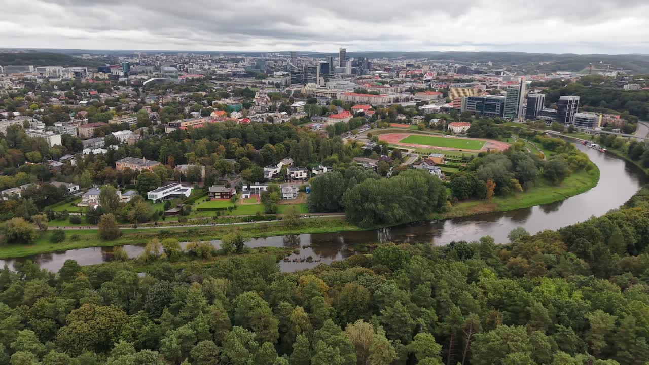 Vista aérea se afastando da margem do rio com árvores e a cidade de Vilnius ao fundo