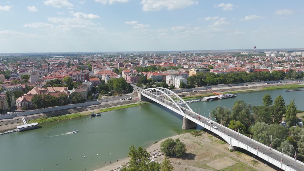 Aerial orbiting Szeged’s Belvárosi Bridge, emphasizing its structure, the flowing Tisza River, and the surrounding urban charm