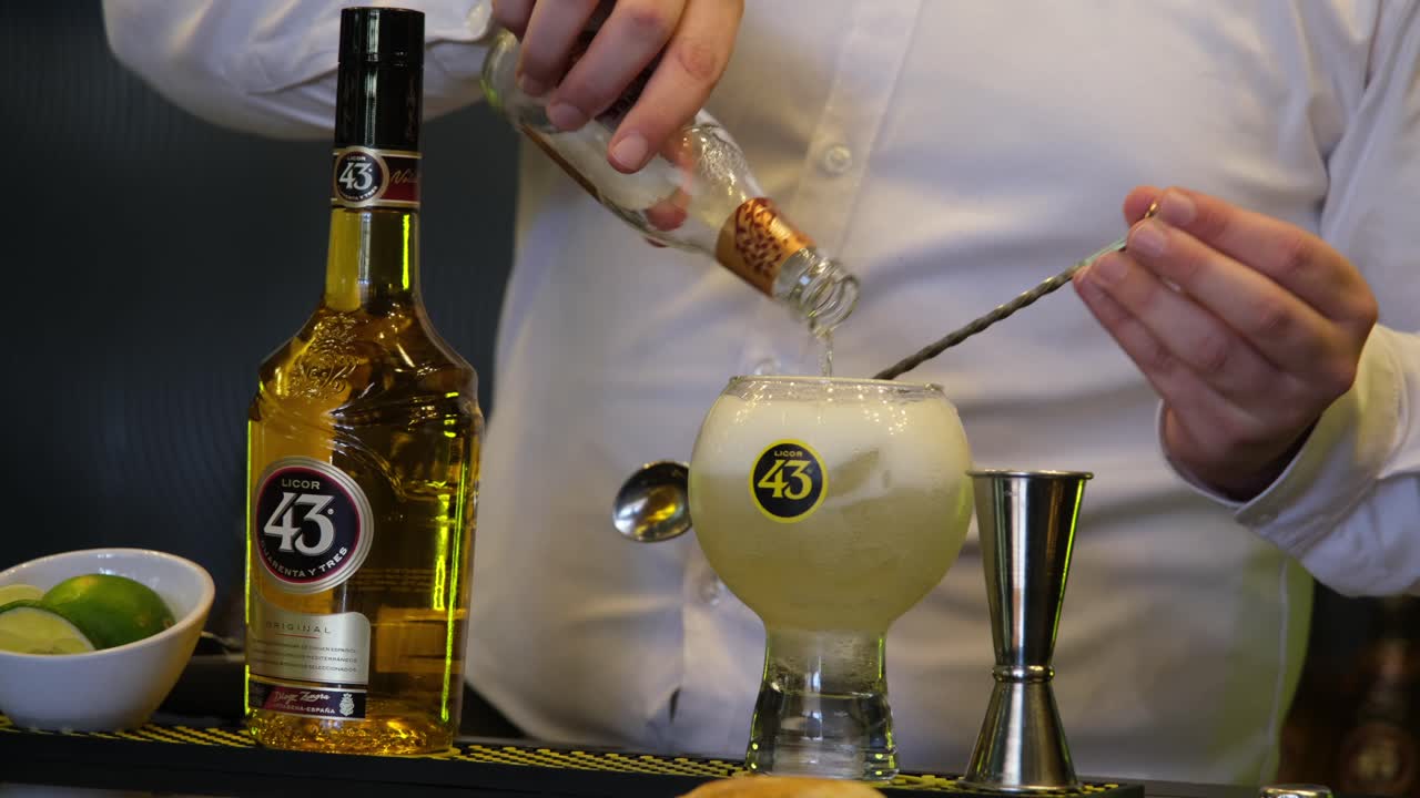A man skillfully prepares cocktails using Licor 43, a renowned Spanish liqueur, showcasing its vibrant flavors in a captivating presentation for an eager audience.
