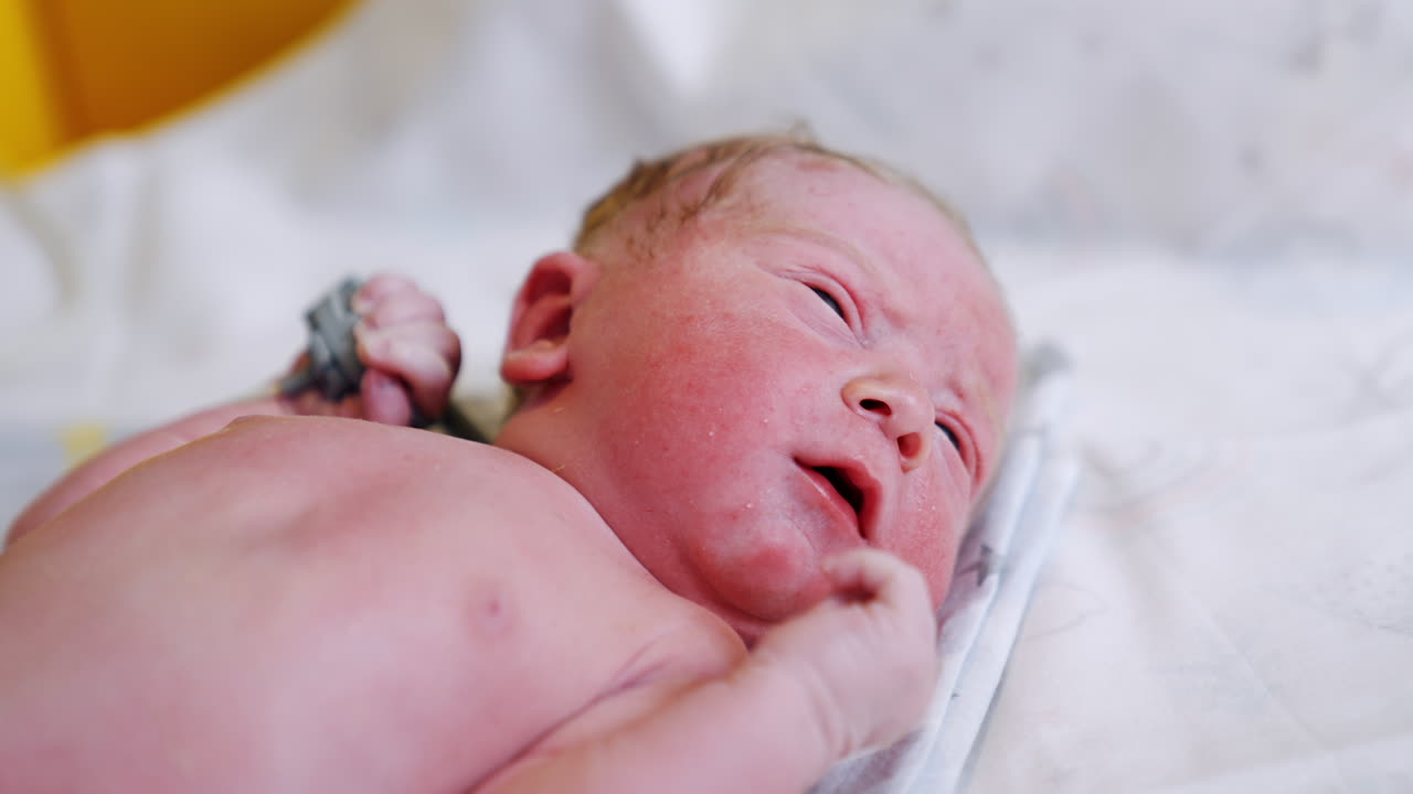 Naked pink Caucasian newborn lying on the back. Lovely baby opening eyes and mouth. Close up.
