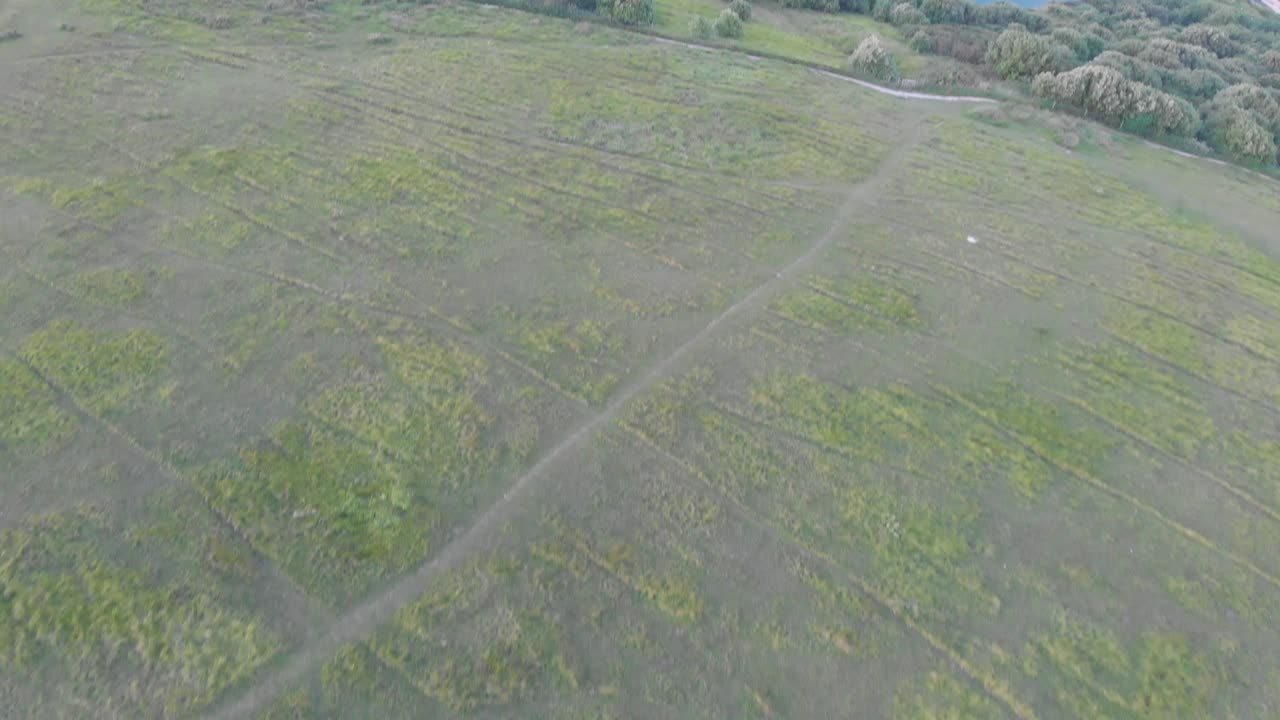 공중 포워드는 모래 해변, 결정 파란 물, 시 보트, 카야키스트 및 바위 절벽에 부히는 파도와 함께 워스 코브의 영상을 보여줍니다.