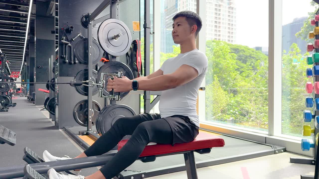 A man exercises on a seated row machine in a brightly lit gym with large windows